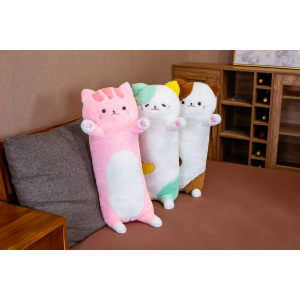 Su un divano grigio in un piccolo soggiorno con pavimento marrone, 3 cuscini di peluche con l'effigie di un grande gatto in piedi sul divano, uno è rosa, il secondo è verde e il terzo è marrone
