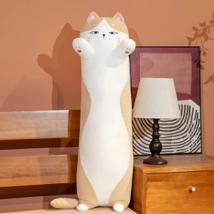 Su un letto con accanto un comodino, con una lampada da comodino bianca e una cornice dietro di essa, c'è un cuscino di gatto bianco e marrone, in piedi sulle sue piccole zampe posteriori