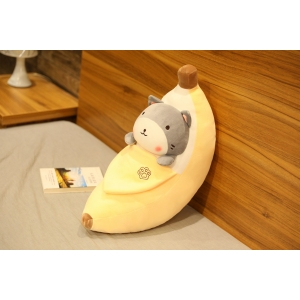 Peluche a forma di banana sbucciata con all'interno uno shiba inu grigio su un letto grigio e una parete color legno con un libro accanto